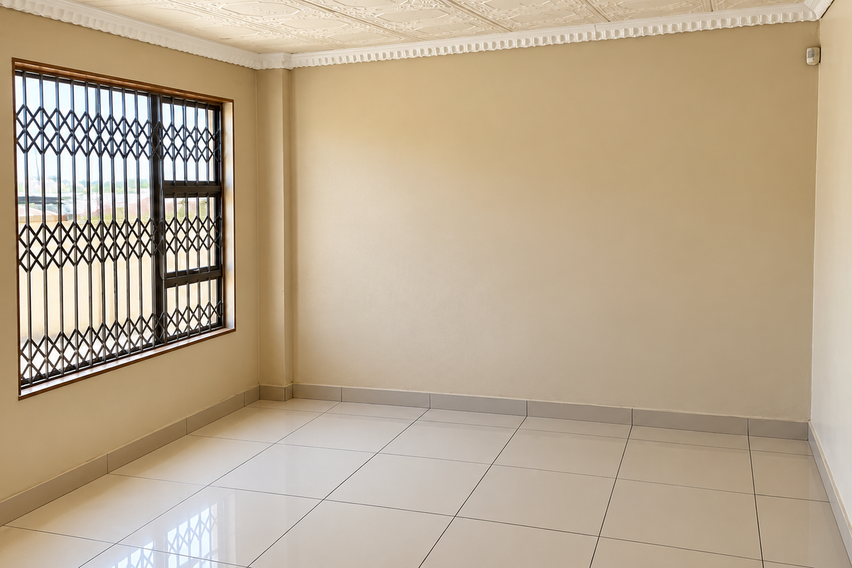 A bright, empty living room featuring neutral tiled flooring, decorative ceiling detailing, and a window fitted with a security gate.