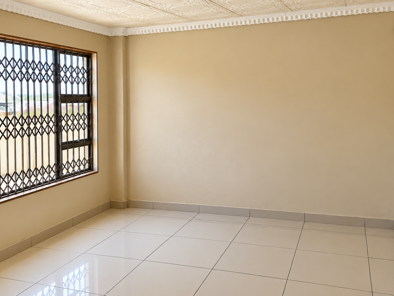 A bright, empty living room featuring neutral tiled flooring, decorative ceiling detailing, and a window fitted with a security gate.