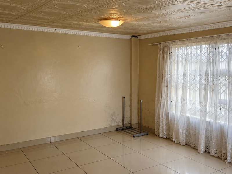 An empty living room featuring tiled floors, decorative ceiling tiles, and a security gate on the window, requiring cosmetic updates to address wall condition.
