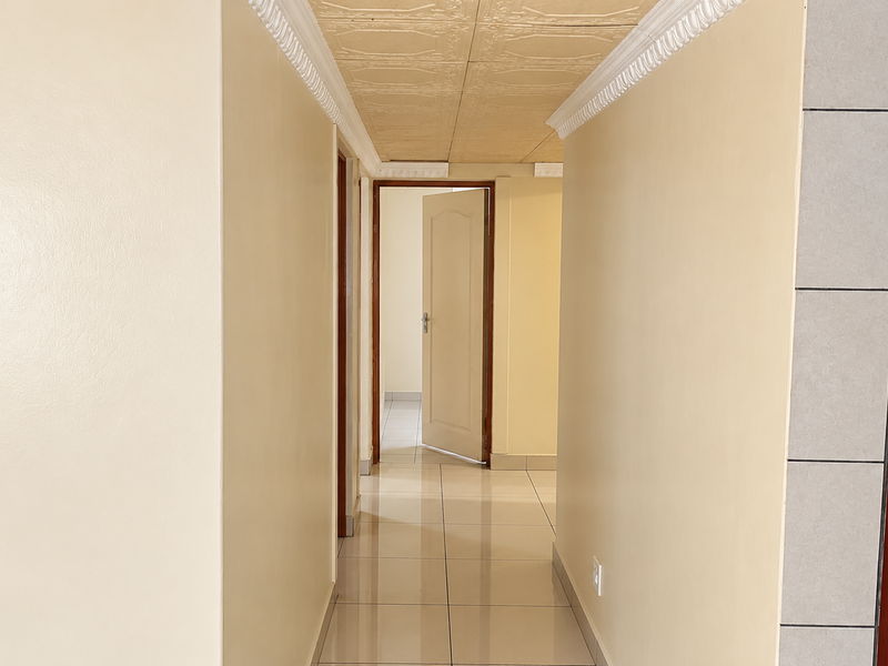 A clean, empty hallway featuring tiled flooring, decorative ceiling panels, and crown molding, providing access to multiple rooms.