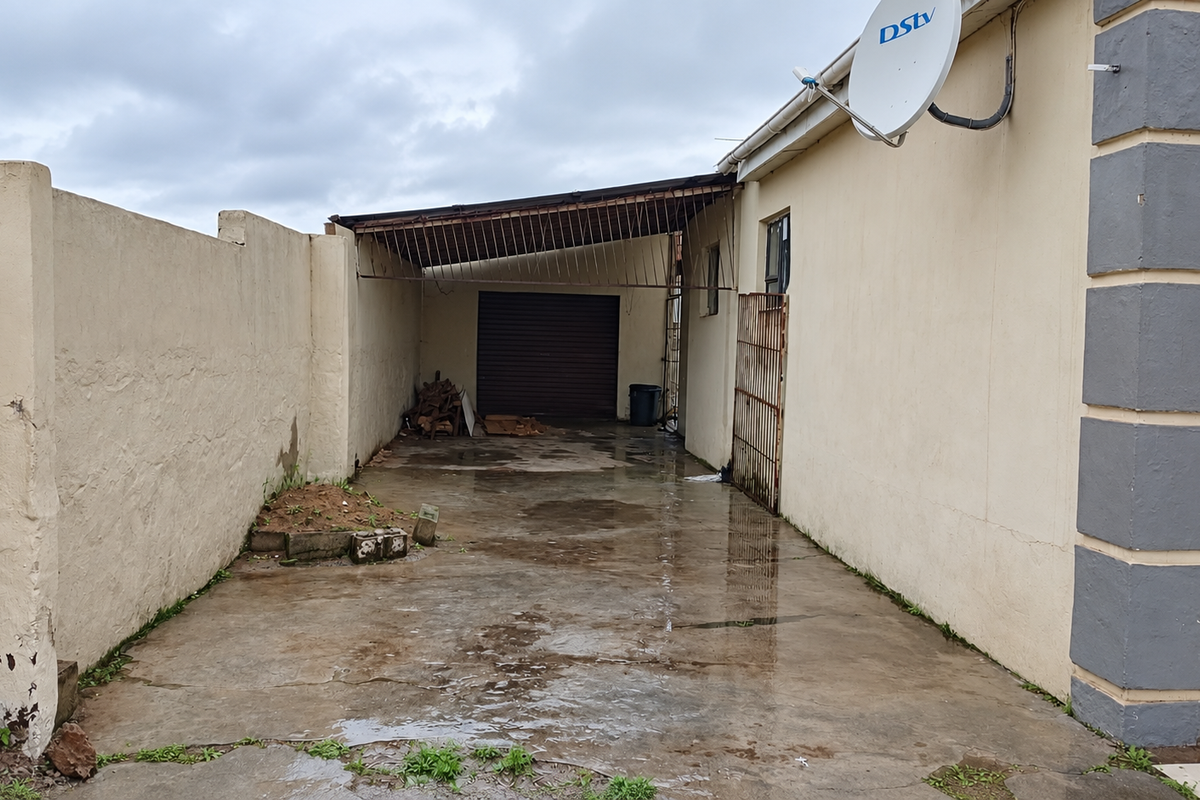 Rear exterior view showing a concrete driveway, perimeter wall, and a covered carport area with a garage door.