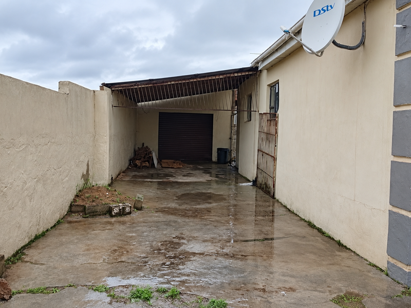 Rear exterior view showing a concrete driveway, perimeter wall, and a covered carport area with a garage door.