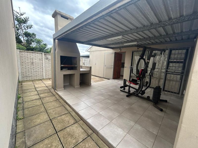 Covered patio area featuring a built-in braai, tiled flooring, and direct access to the interior, providing a functional outdoor entertainment space.