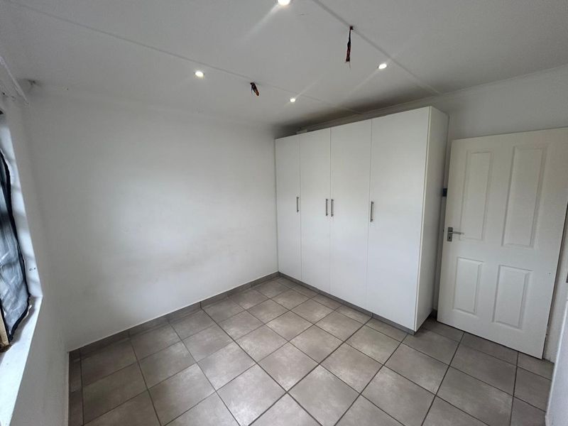 An empty bedroom featuring tiled flooring, built-in cupboards, and recessed ceiling lighting.