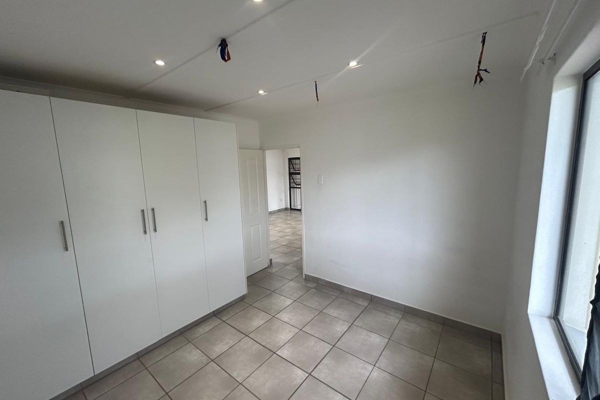 An empty bedroom featuring tiled flooring, built-in cupboards, and recessed downlighting, with some exposed electrical wiring visible on the ceiling.