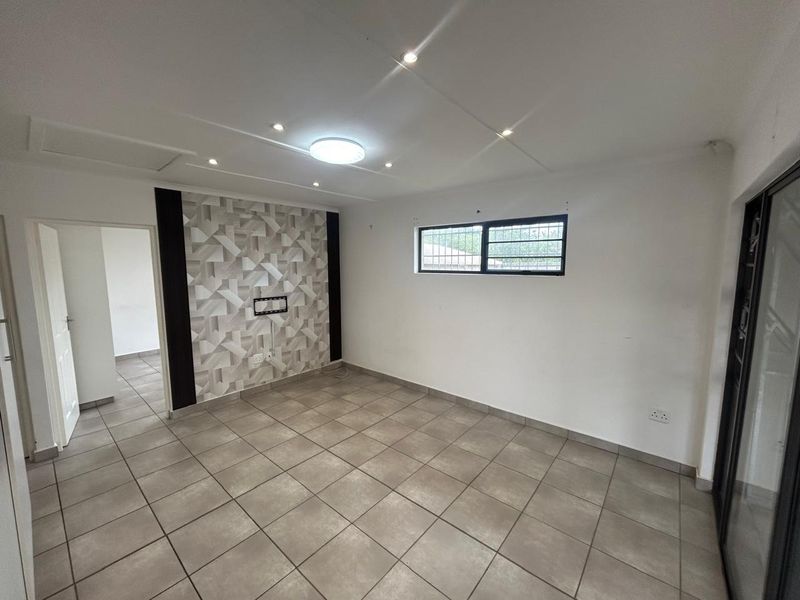 An empty living room featuring tiled flooring, recessed downlighting, and a decorative feature wall with a mounted television bracket.