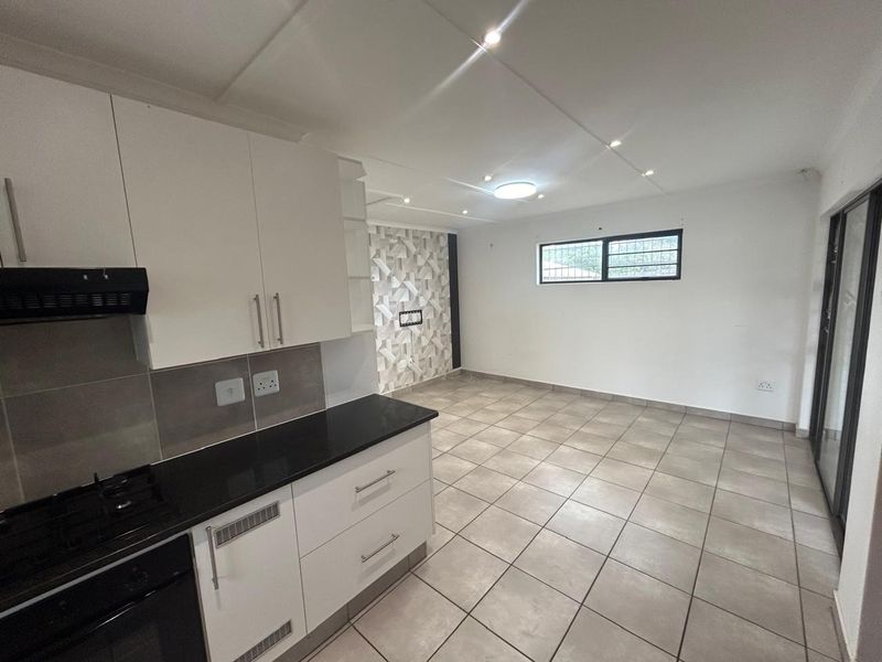 Open-plan kitchen and living area featuring modern white cabinetry, black granite countertops, tiled flooring, and recessed lighting in a clean, vacant space.