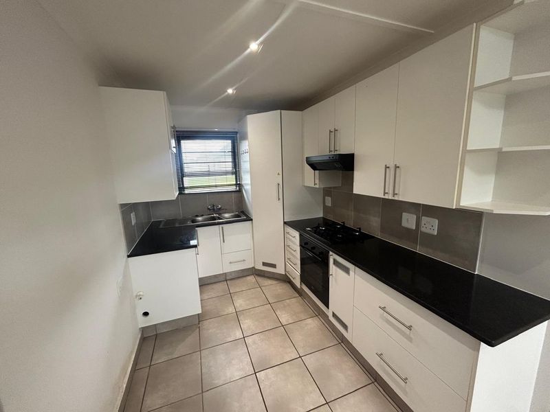 A clean and functional kitchen featuring white cabinetry, black granite countertops, built-in oven, gas hob, and tiled flooring.
