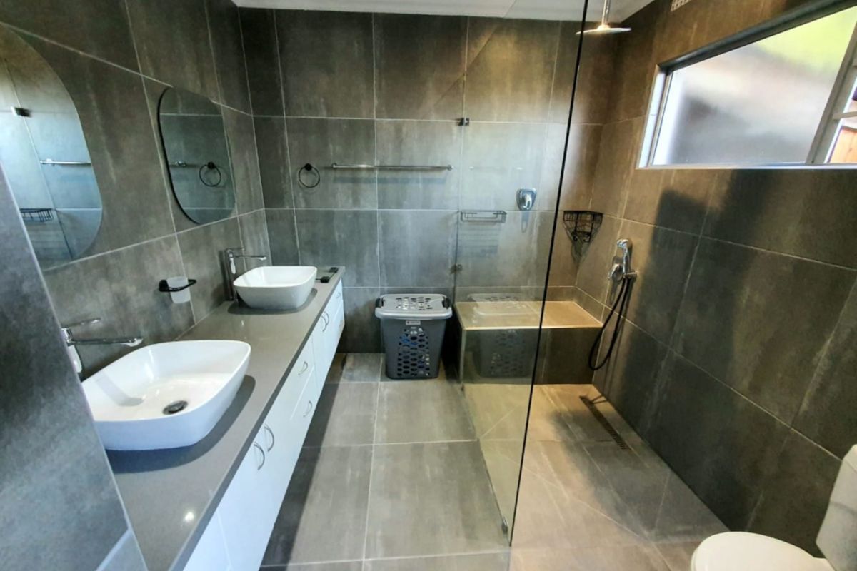 Modern bathroom featuring a double vanity with vessel sinks, a spacious walk-in shower with a glass screen, and contemporary floor-to-ceiling tiling.