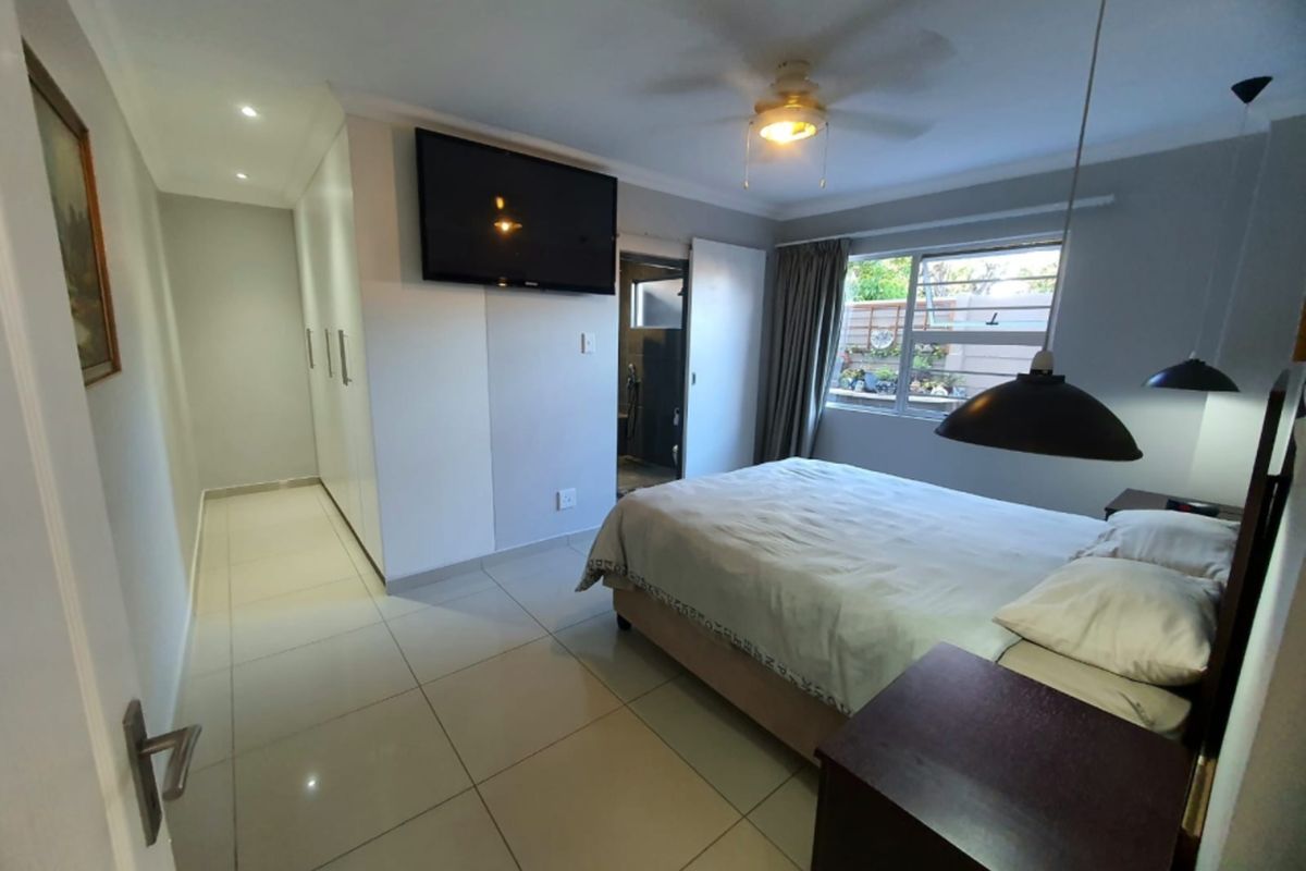 A well-maintained bedroom featuring tiled flooring, built-in cupboards, a ceiling fan, and recessed lighting, with an en-suite bathroom access.