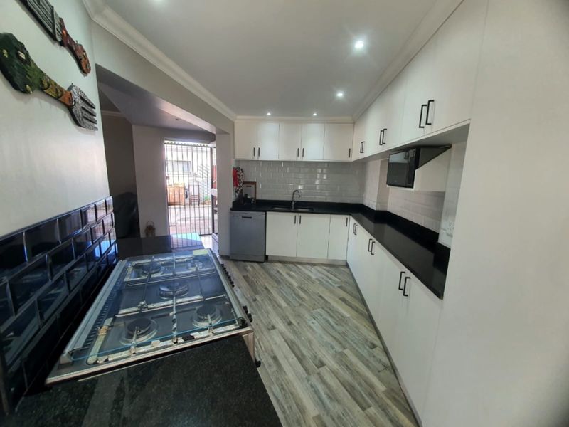 Modern kitchen featuring white cabinetry, black granite countertops, subway tile backsplash, and a gas hob with integrated appliances.