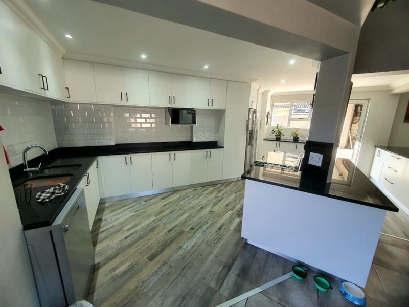 Modern kitchen featuring white cabinetry, contrasting black stone countertops, subway tile backsplash, and a functional island layout with recessed lighting.