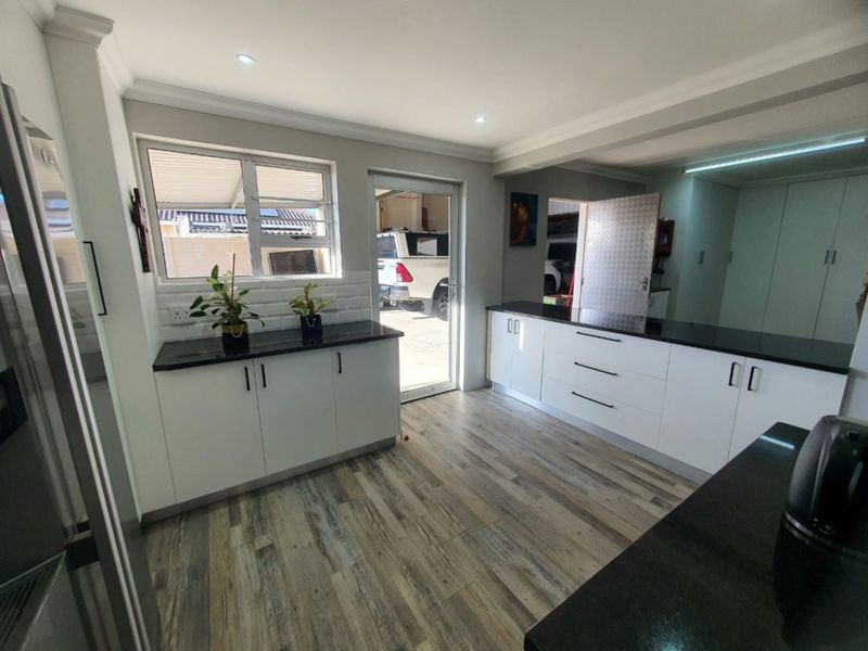 Modern kitchen featuring white built-in cabinetry, contrasting black granite countertops, laminate flooring, and recessed lighting, with direct access to the exterior.