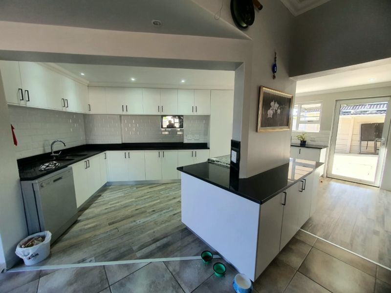 Modern kitchen featuring white cabinetry, contrasting black stone countertops, subway tile backsplash, and durable wood-look flooring with an open-plan layout.