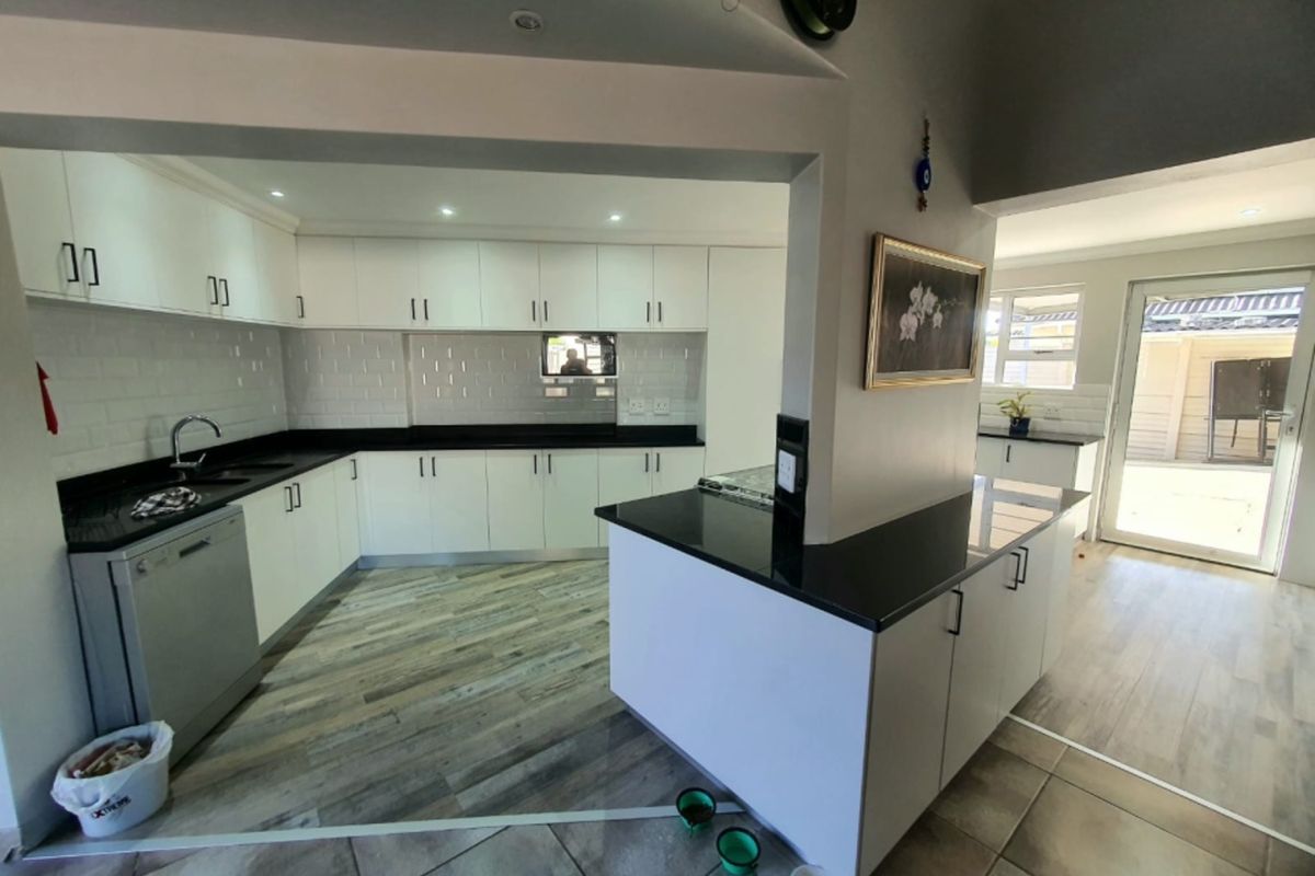 Modern kitchen featuring white cabinetry, contrasting black stone countertops, subway tile backsplash, and durable wood-look flooring with an open-plan layout.
