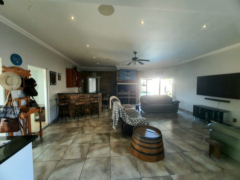 Spacious open-plan living area featuring a built-in brick bar, fireplace, tiled flooring, and recessed lighting, offering a versatile space for entertainment and relaxation.