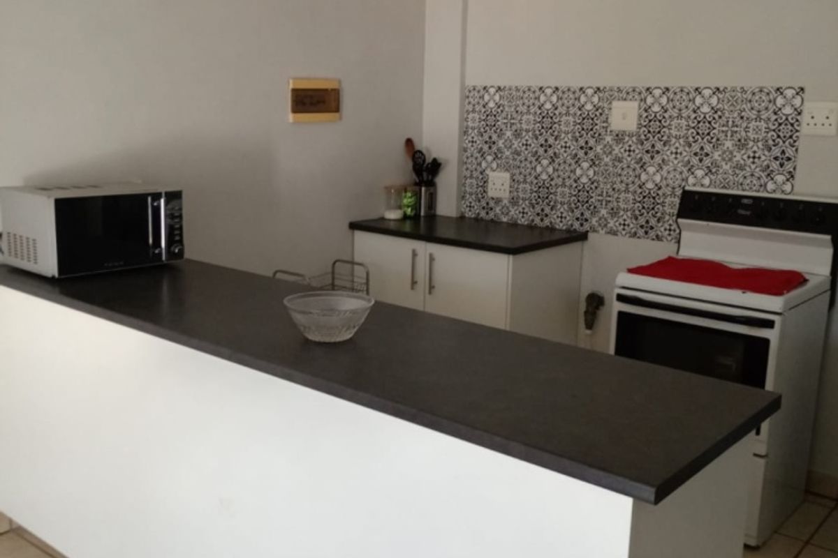 A functional kitchen featuring a breakfast bar, dark laminate countertops, patterned tile backsplash, and a freestanding stove with ceramic floor tiles.