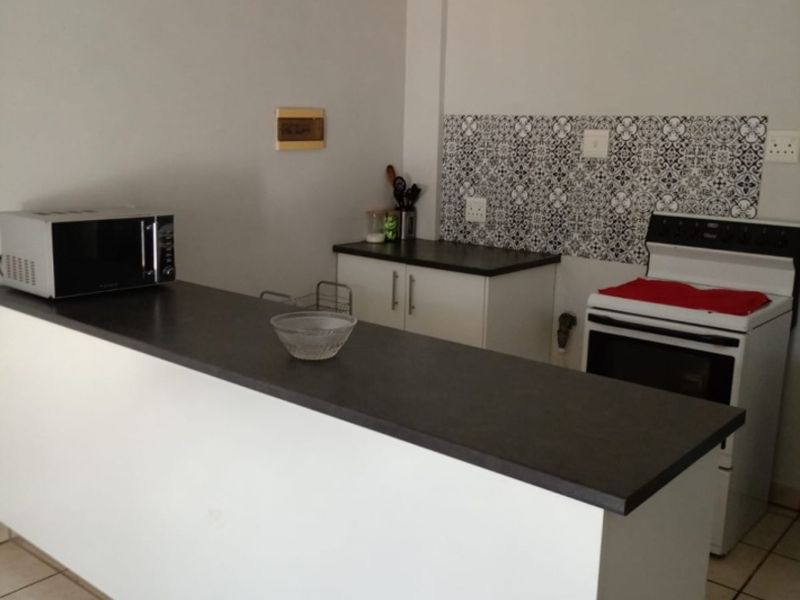A functional kitchen featuring a breakfast bar, dark laminate countertops, patterned tile backsplash, and a freestanding stove with ceramic floor tiles.