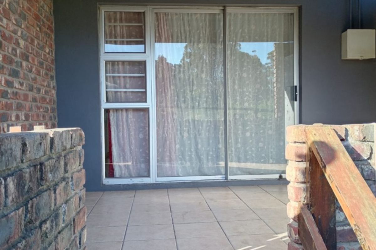 A covered patio area featuring tiled flooring, brick walls, and a sliding glass door entrance, providing a functional outdoor space.