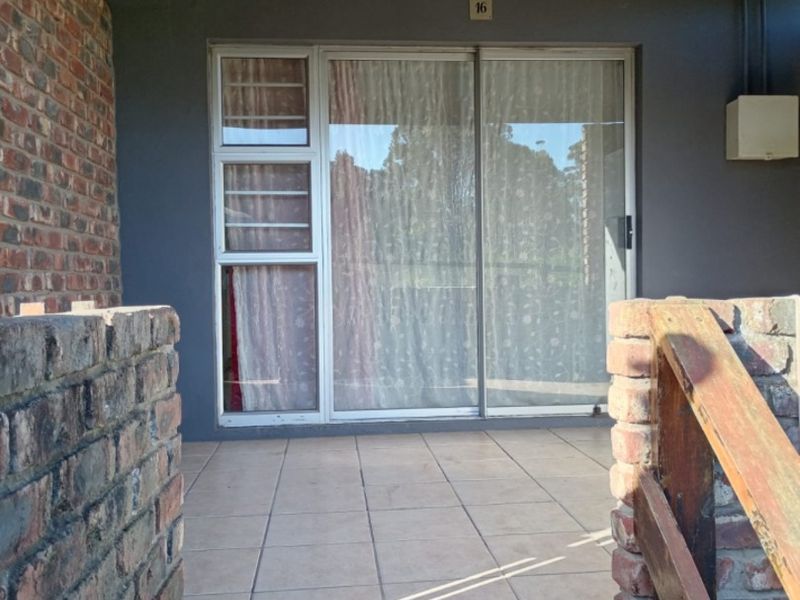 A covered patio area featuring tiled flooring, brick walls, and a sliding glass door entrance, providing a functional outdoor space.