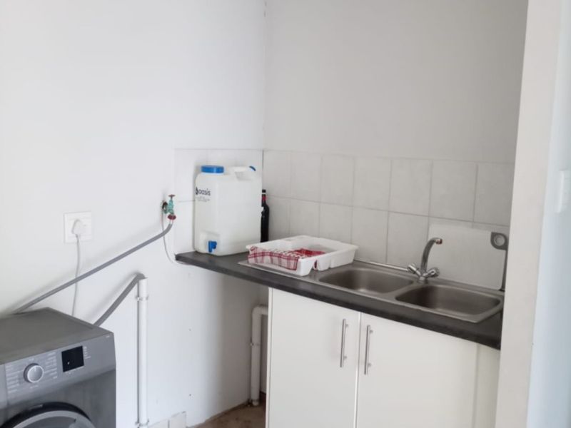 A functional laundry area featuring a built-in sink, base cabinetry, tiled splashback, and dedicated plumbing connections for a washing machine.