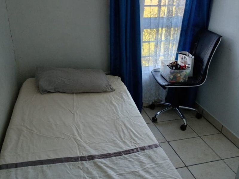 A compact bedroom featuring tiled flooring and a window with security bars, providing a functional space for a single bed.