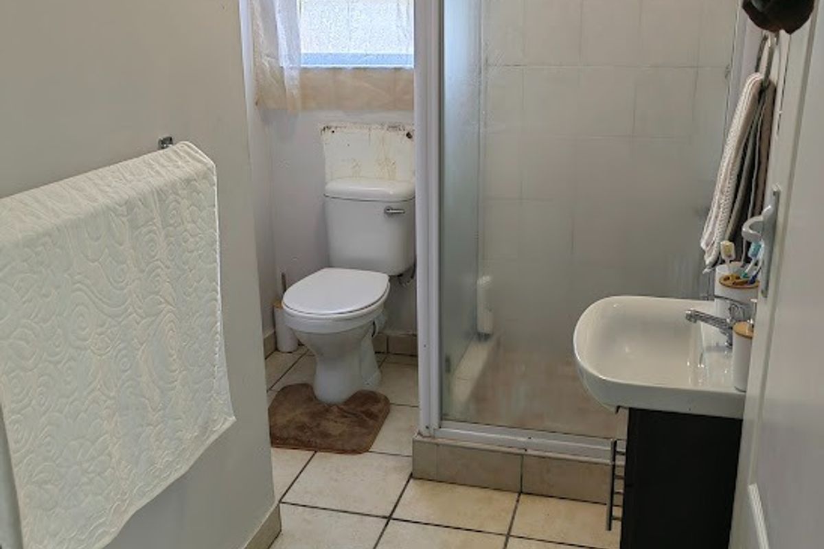 A compact bathroom featuring a shower enclosure, toilet, and vanity basin with tiled flooring and a window.