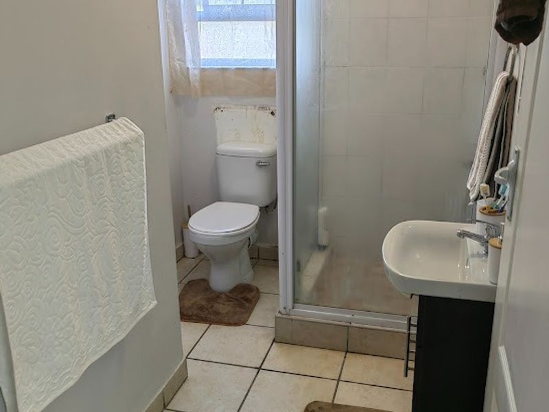 A compact bathroom featuring a shower enclosure, toilet, and vanity basin with tiled flooring and a window.