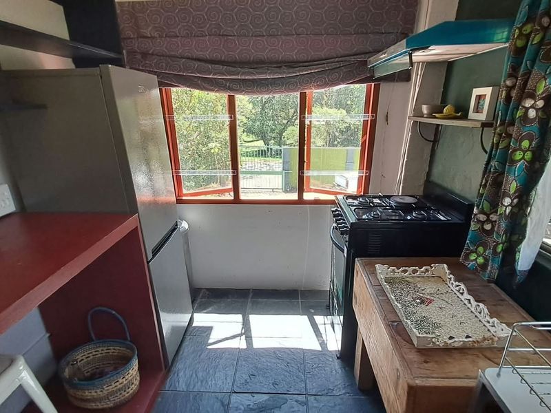 Compact kitchen featuring a gas stove, extractor fan, tiled flooring, and built-in shelving with views through casement windows.