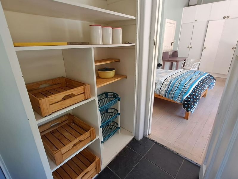 A functional scullery or storage area with built-in shelving, leading into a bedroom featuring built-in cupboards and light-toned flooring.