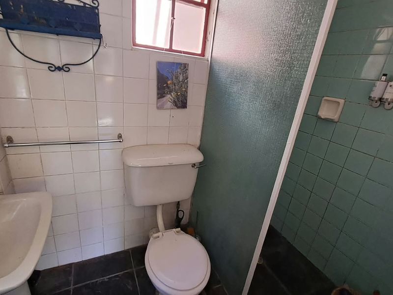 A compact bathroom featuring a pedestal basin, toilet, and a separate shower enclosure with tiled walls and flooring, requiring cosmetic updates.