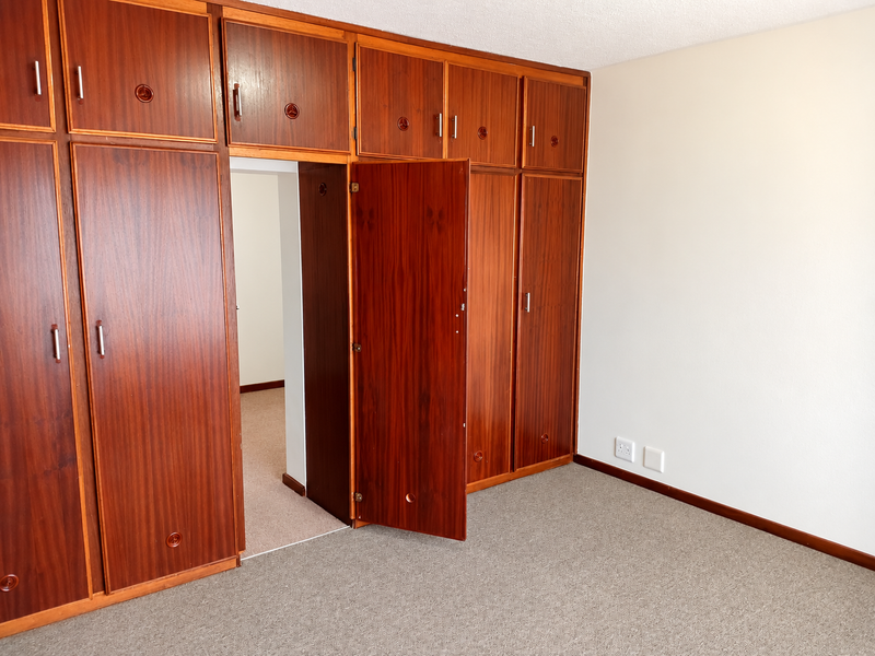 A bedroom featuring extensive built-in wooden cupboards, neutral wall finishes, and carpeted flooring, offering a functional and spacious layout.