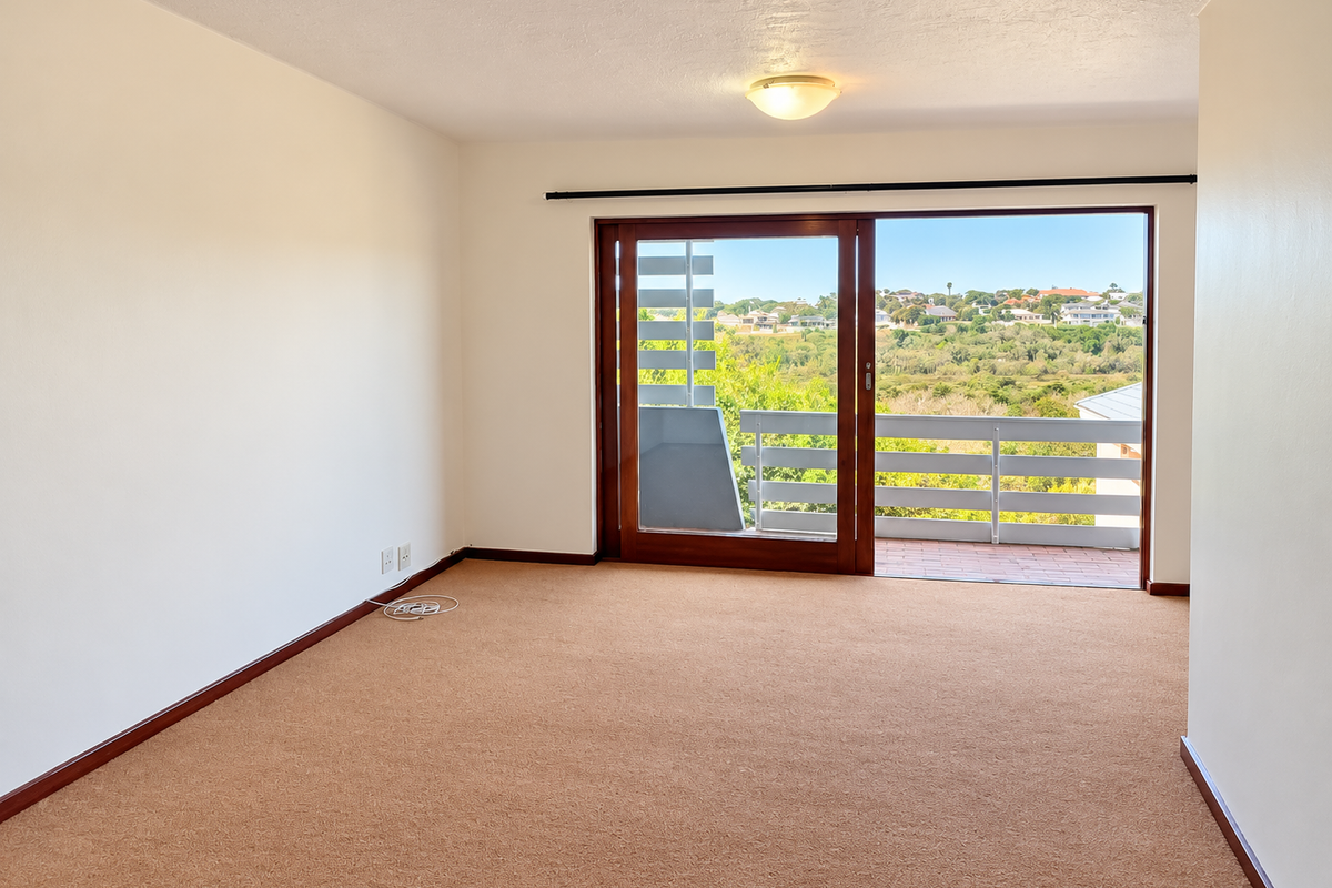 An empty bedroom featuring neutral carpeting, a ceiling light fixture, and a large sliding glass door providing access to a balcony with scenic views.