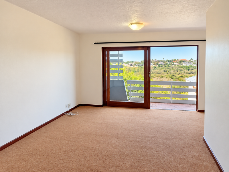 An empty bedroom featuring neutral carpeting, a ceiling light fixture, and a large sliding glass door providing access to a balcony with scenic views.