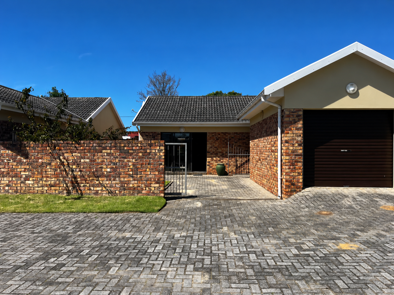 Front view of a townhouse featuring a brick facade, tiled roof, paved driveway, and a single garage.