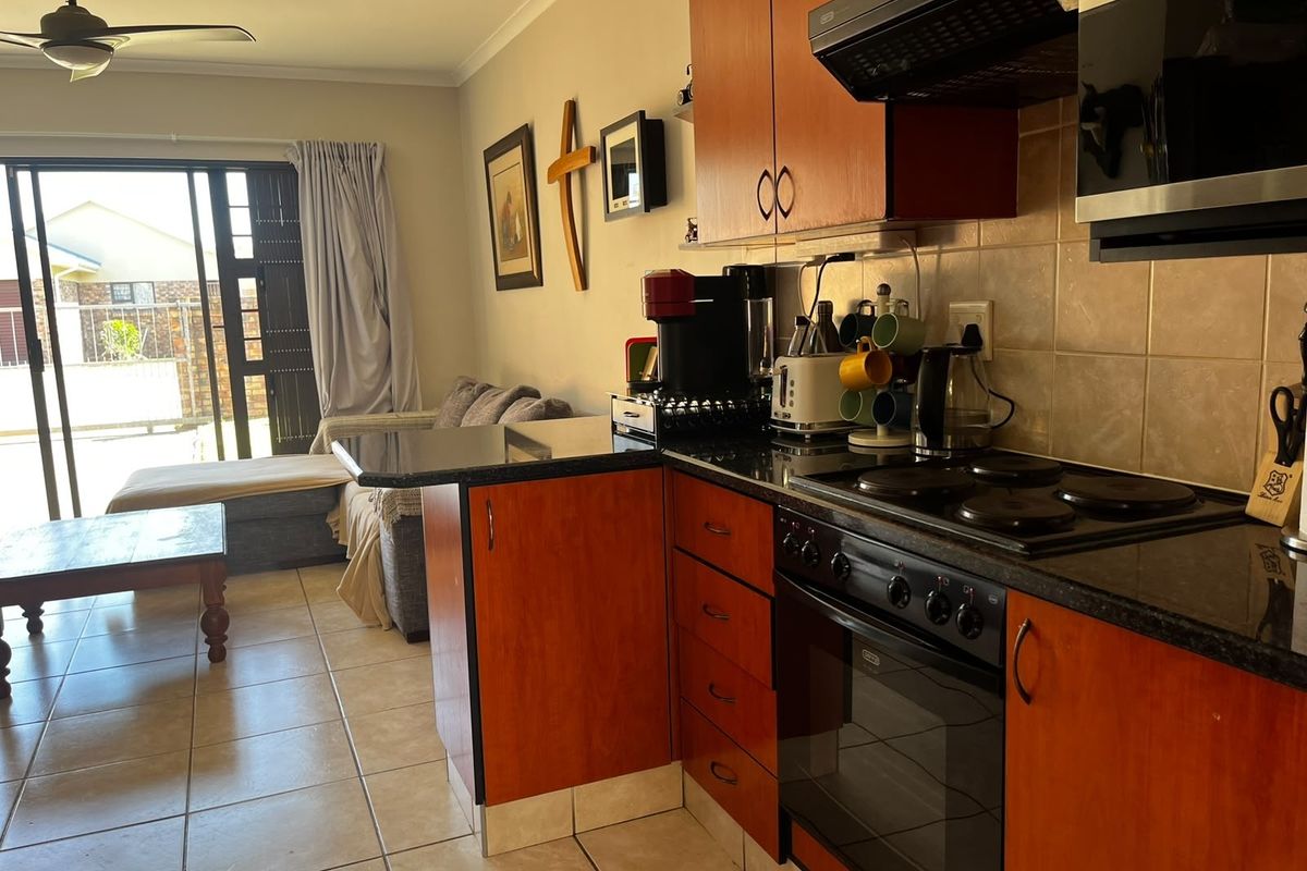 Open-plan kitchen and living area featuring wood-finish cabinetry, granite countertops, built-in appliances, and direct access to an outdoor patio through sliding glass doors.