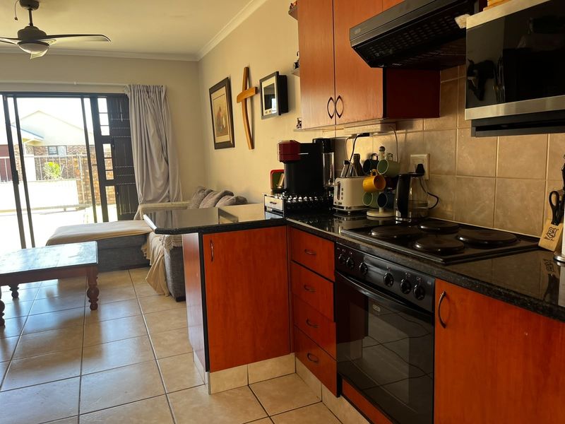 Open-plan kitchen and living area featuring wood-finish cabinetry, granite countertops, built-in appliances, and direct access to an outdoor patio through sliding glass doors.