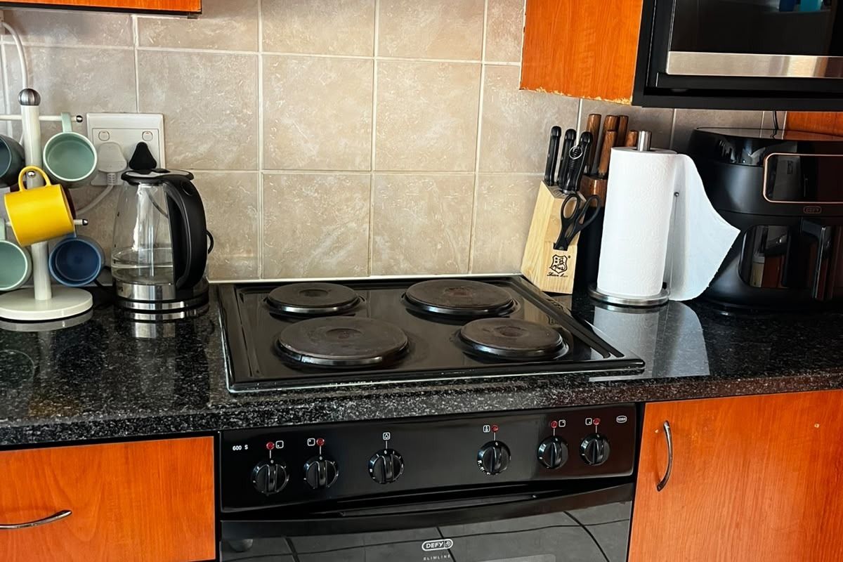 A functional kitchen area featuring wooden cabinetry, granite countertops, a built-in oven, electric hob, and a tiled backsplash.