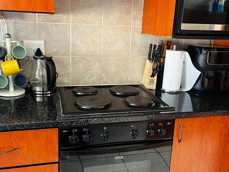 A functional kitchen area featuring wooden cabinetry, granite countertops, a built-in oven, electric hob, and a tiled backsplash.