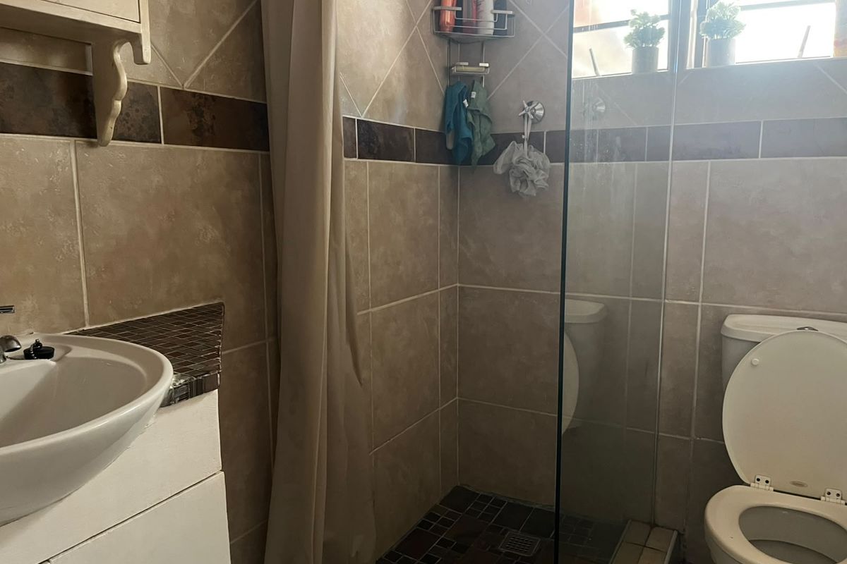 A functional bathroom featuring a vanity basin, a shower enclosure with a glass screen, and a toilet, finished with neutral wall and floor tiling.