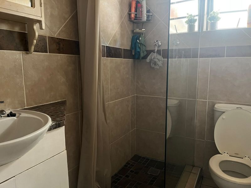 A functional bathroom featuring a vanity basin, a shower enclosure with a glass screen, and a toilet, finished with neutral wall and floor tiling.