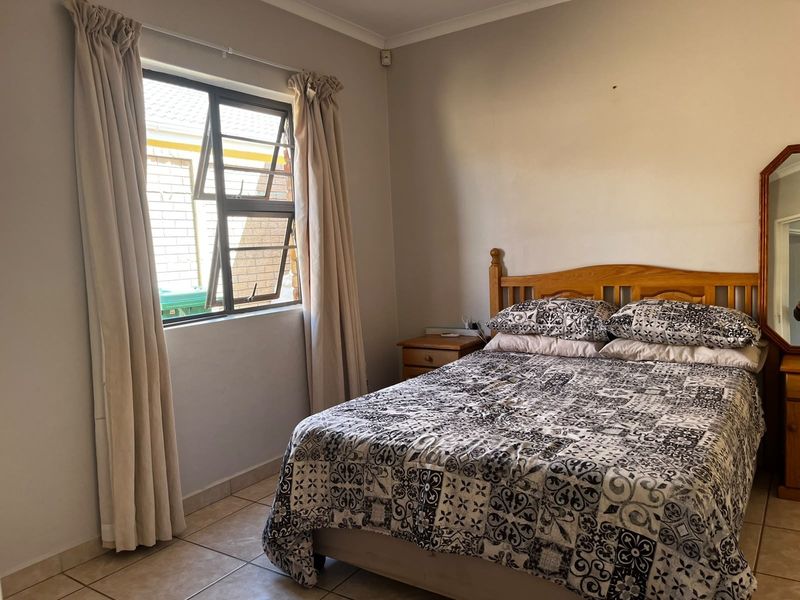 A functional bedroom featuring tiled flooring and a window with aluminium frames, offering a neutral base for potential interior updates.