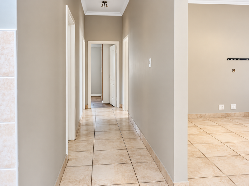 A clean, neutral-toned hallway featuring tiled flooring and coved ceilings, providing access to multiple rooms within the property.