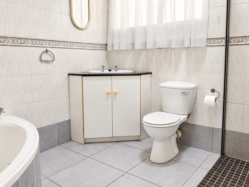 A functional bathroom featuring a corner vanity, built-in bathtub, and separate shower area with neutral wall and floor tiling.