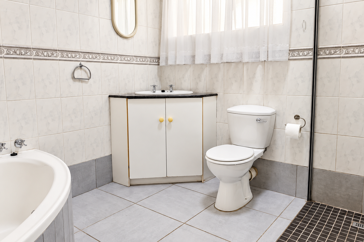 A functional bathroom featuring a corner vanity, built-in bathtub, and separate shower area with neutral wall and floor tiling.