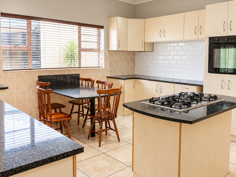 A functional kitchen featuring light wood cabinetry, granite countertops, a central island with a gas hob, and a built-in oven.