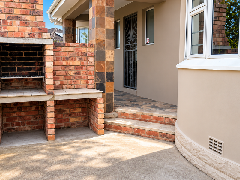 A well-maintained outdoor patio area featuring a built-in brick braai, tiled steps, and a secure entrance to the main dwelling.