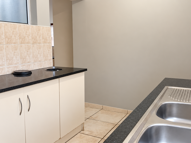 A clean, functional kitchen area featuring neutral cabinetry, dark countertops, and a double stainless steel sink with tiled splashbacks and flooring.