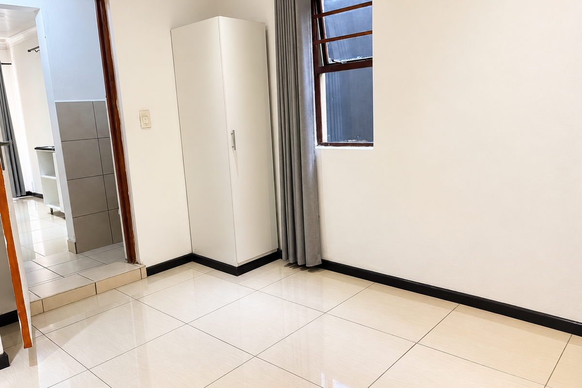 A clean, empty bedroom featuring neutral tiled flooring, a built-in wardrobe, and a window, offering a bright and versatile living space.