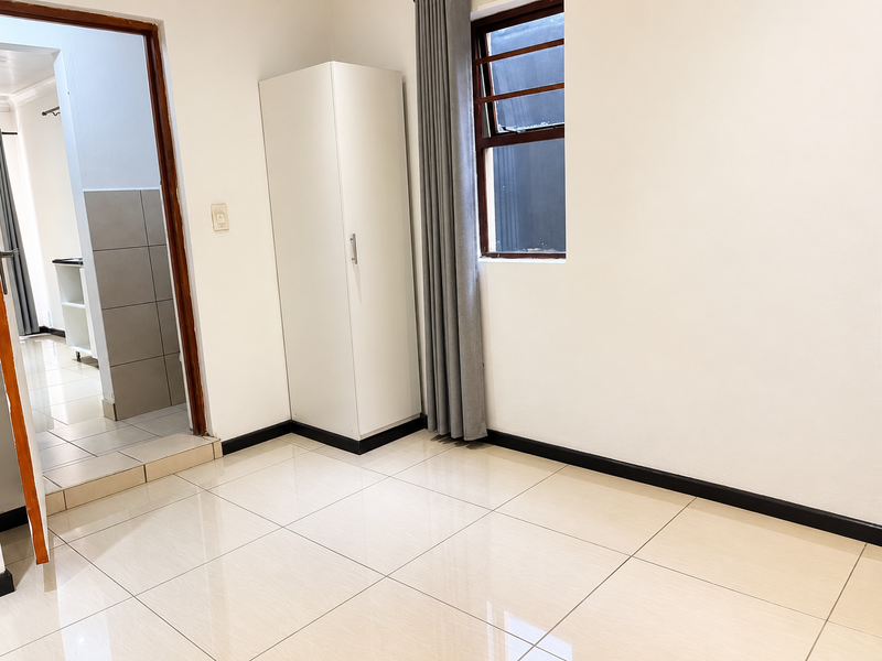 A clean, empty bedroom featuring neutral tiled flooring, a built-in wardrobe, and a window, offering a bright and versatile living space.